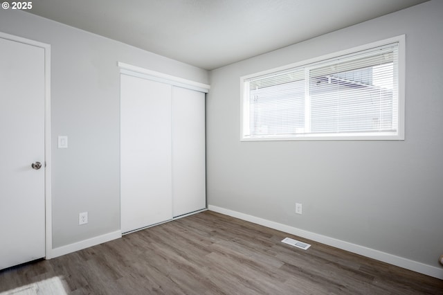 unfurnished bedroom featuring a closet, wood finished floors, visible vents, and baseboards