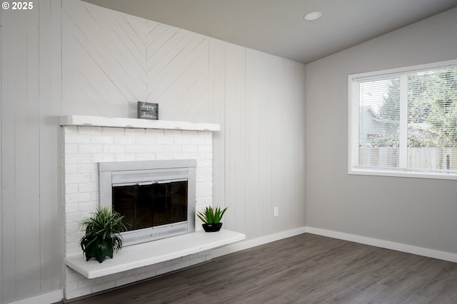 unfurnished living room with vaulted ceiling, dark wood-type flooring, a brick fireplace, and baseboards