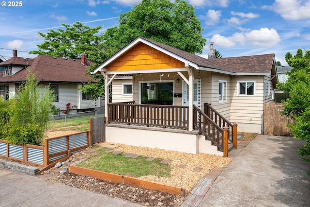 view of front of house with covered porch, roof with shingles, and fence