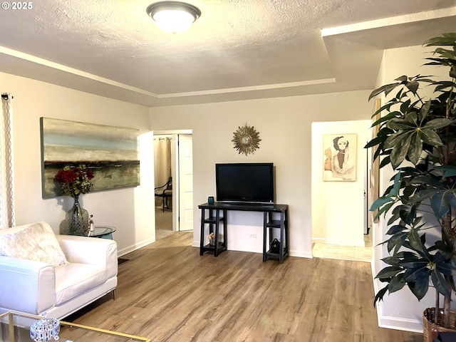 living room featuring a tray ceiling, a textured ceiling, baseboards, and wood finished floors