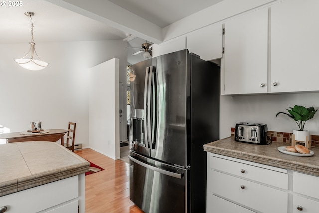 kitchen with stainless steel fridge, tasteful backsplash, light hardwood / wood-style floors, white cabinets, and decorative light fixtures