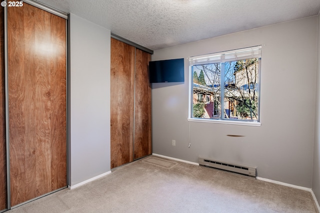 unfurnished bedroom with multiple closets, a baseboard heating unit, light colored carpet, and a textured ceiling