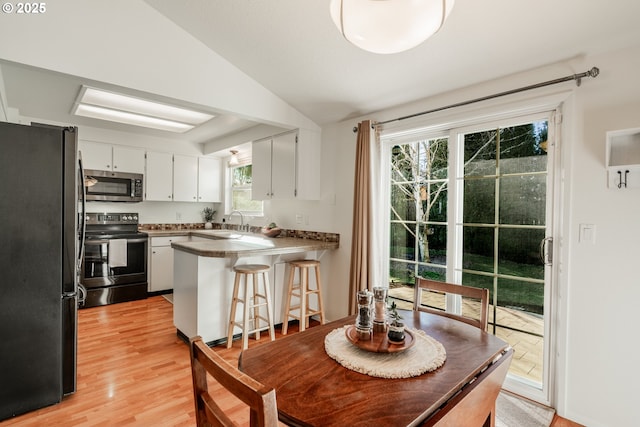 kitchen featuring lofted ceiling, white cabinetry, black fridge, kitchen peninsula, and electric stove