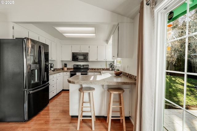 kitchen with white cabinetry, a kitchen breakfast bar, kitchen peninsula, and black appliances