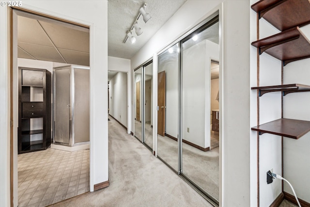 hallway featuring light carpet, rail lighting, baseboards, and a textured ceiling