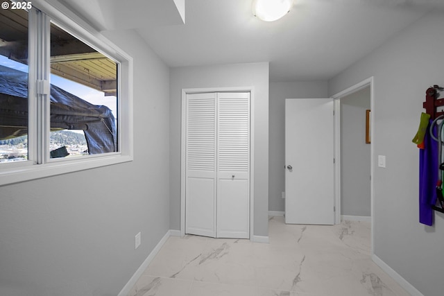 unfurnished bedroom with marble finish floor, baseboards, and a closet