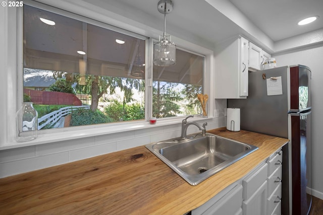 kitchen with pendant lighting, white cabinetry, a sink, and wooden counters