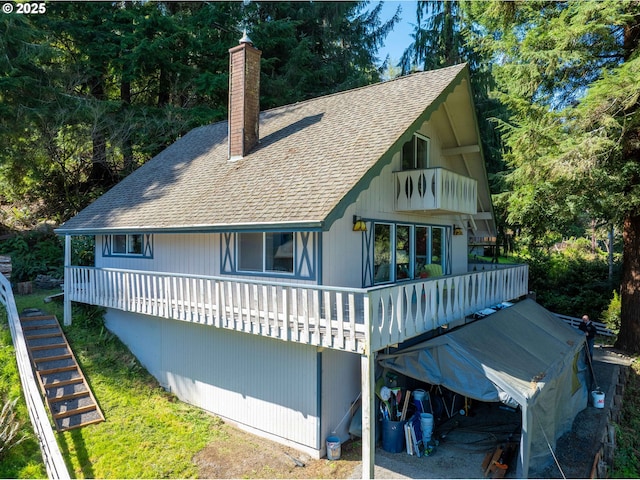 rear view of property featuring a wooden deck, a chimney, and roof with shingles