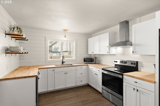 kitchen featuring stainless steel appliances, hanging light fixtures, wooden counters, a sink, and wall chimney range hood