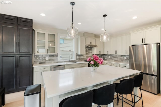 kitchen with appliances with stainless steel finishes, a sink, light countertops, a breakfast bar area, and recessed lighting