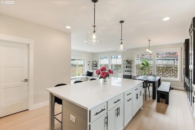 kitchen featuring light wood-type flooring, a breakfast bar, baseboards, a center island, and recessed lighting