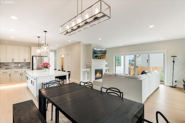 dining room with light wood finished floors, a glass covered fireplace, recessed lighting, and baseboards