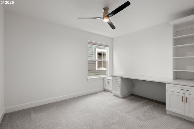 unfurnished office with built in desk, ceiling fan, and light carpet