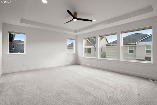 empty room featuring ceiling fan, a tray ceiling, and light carpet