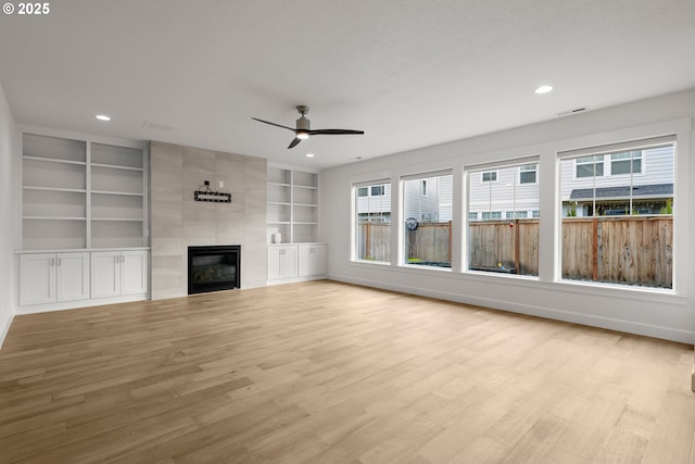 unfurnished living room with light wood-type flooring, a fireplace, built in features, and ceiling fan