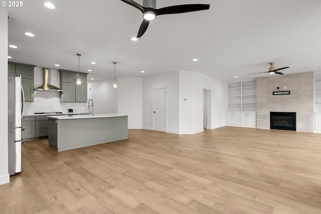 unfurnished living room featuring ceiling fan, light hardwood / wood-style floors, a tile fireplace, and built in shelves