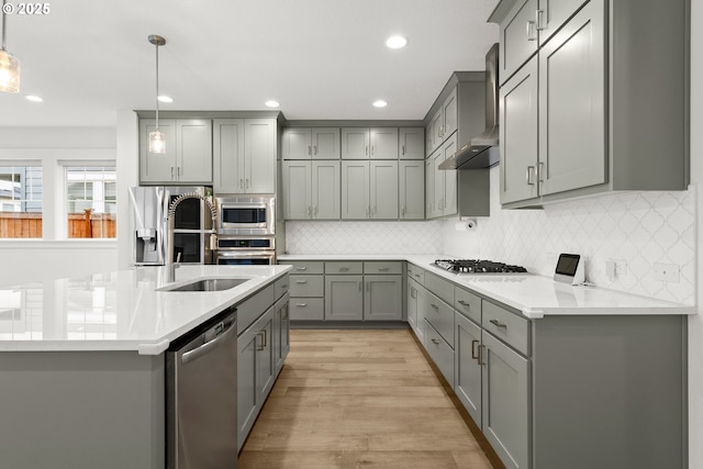 kitchen with hanging light fixtures, wall chimney range hood, gray cabinetry, and stainless steel appliances