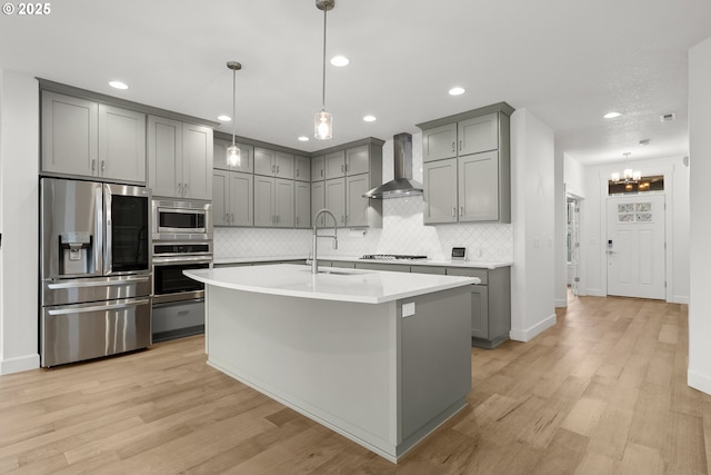 kitchen with stainless steel appliances, wall chimney exhaust hood, pendant lighting, and sink