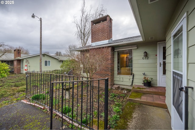 view of home's exterior with brick siding, a chimney, and fence