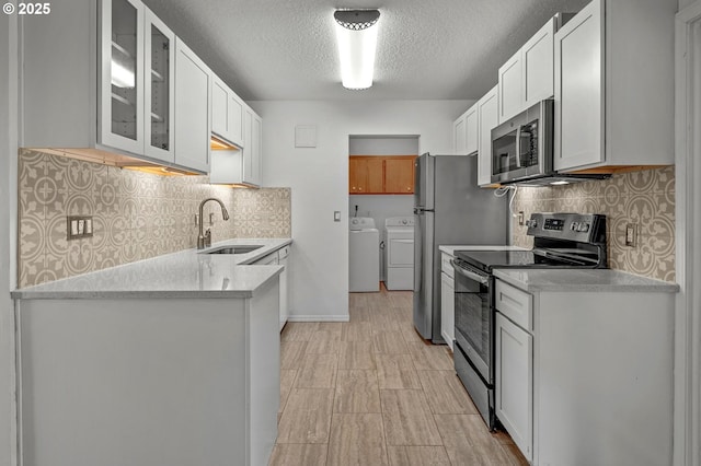 kitchen with washer and dryer, light countertops, white cabinets, a sink, and stainless steel appliances