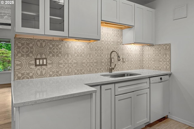 kitchen with a sink, dishwasher, wood finished floors, backsplash, and glass insert cabinets