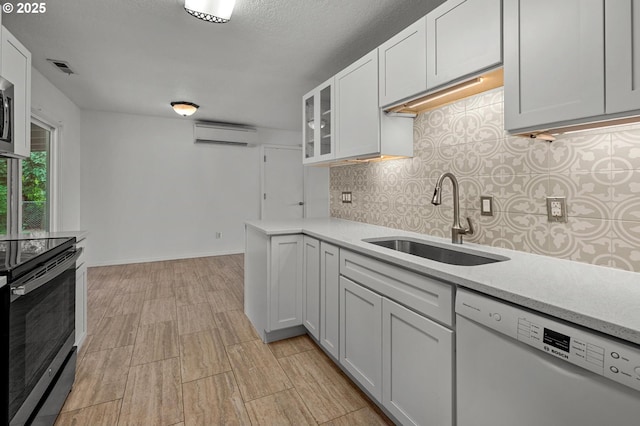 kitchen featuring decorative backsplash, a wall mounted AC, a sink, light wood finished floors, and stainless steel appliances