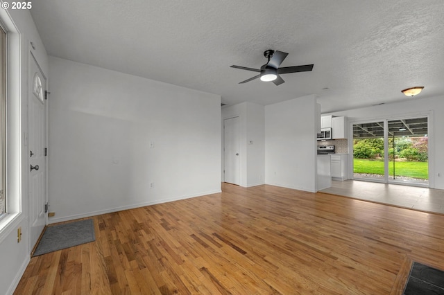 unfurnished living room with light wood-style floors, baseboards, ceiling fan, and a textured ceiling