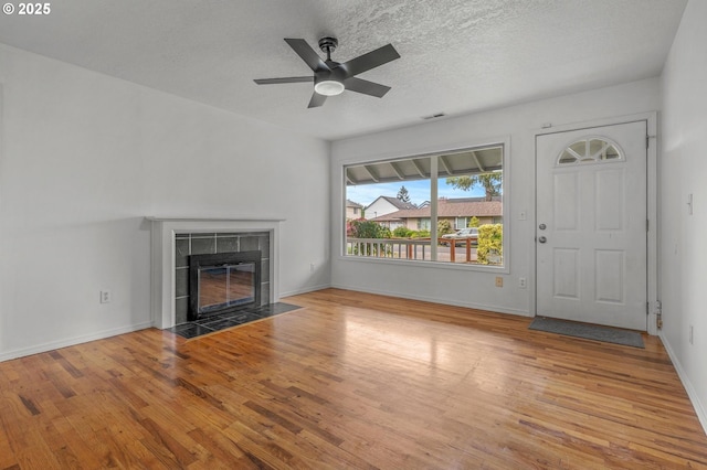 unfurnished living room with a tiled fireplace, a ceiling fan, wood finished floors, and visible vents
