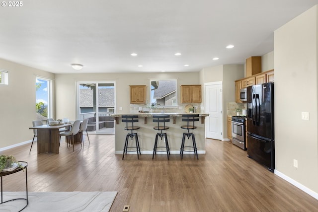 3678 Snowberry Rd, Eugene, OR 97403 - kitchen featuring appliances with stainless steel finishes, a kitchen bar, wood finished floors, tasteful backsplash, and recessed lighting