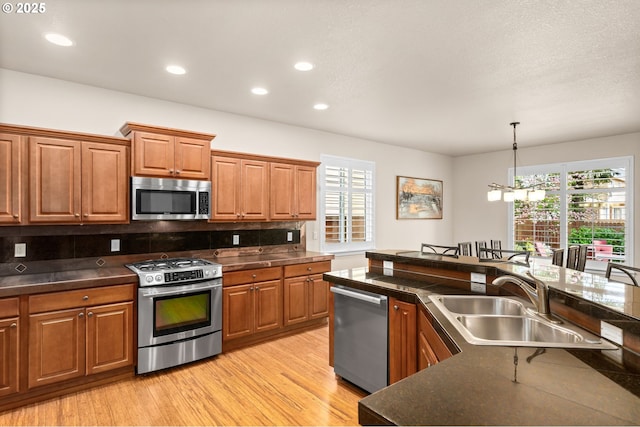 kitchen with appliances with stainless steel finishes, dark countertops, brown cabinets, a sink, and light wood-style floors
