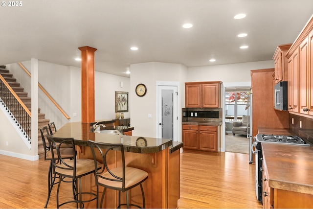 kitchen with dark countertops, appliances with stainless steel finishes, a breakfast bar, brown cabinetry, and light wood-style flooring