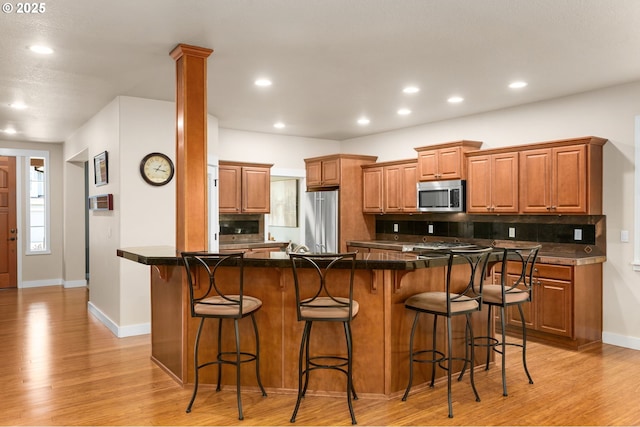 kitchen with brown cabinetry, decorative backsplash, light wood finished floors, and appliances with stainless steel finishes
