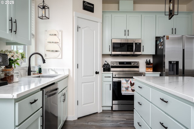 kitchen featuring light stone countertops, decorative light fixtures, dark wood finished floors, appliances with stainless steel finishes, and a sink