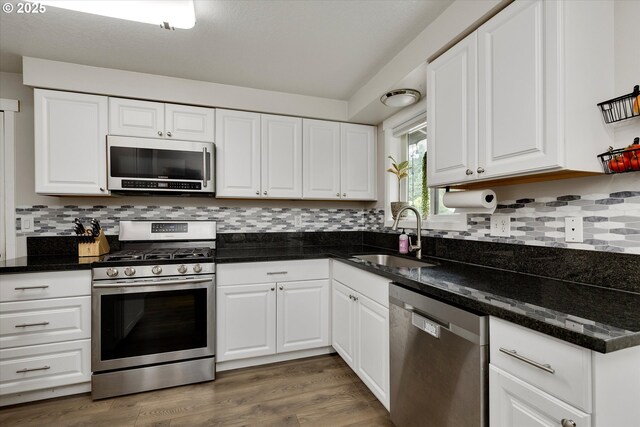 7353 SE Thiessen Rd, Milwaukie, OR 97267 - kitchen with appliances with stainless steel finishes, white cabinets, backsplash, wood finished floors, and dark stone counters