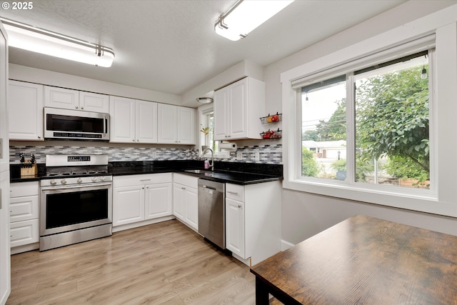 7353 SE Thiessen Rd, Milwaukie, OR 97267 - kitchen with appliances with stainless steel finishes, dark countertops, decorative backsplash, white cabinets, and light wood-style floors