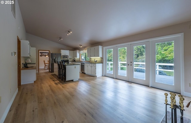 kitchen with dark countertops, stainless steel appliances, white cabinets, light wood-style floors, and lofted ceiling