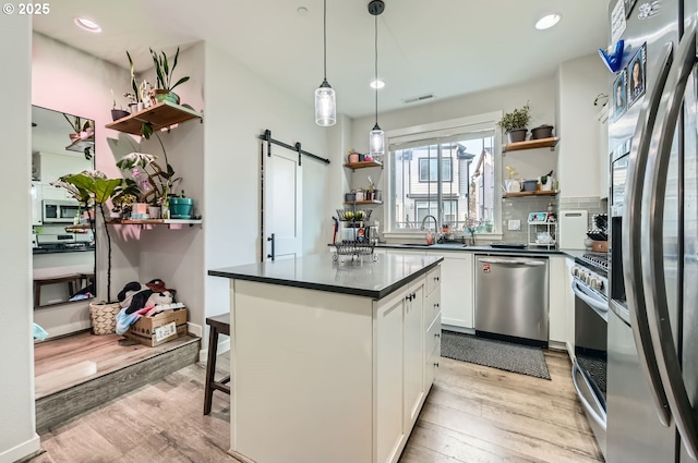 kitchen with light hardwood / wood-style flooring, stainless steel appliances, a barn door, white cabinetry, and a kitchen breakfast bar