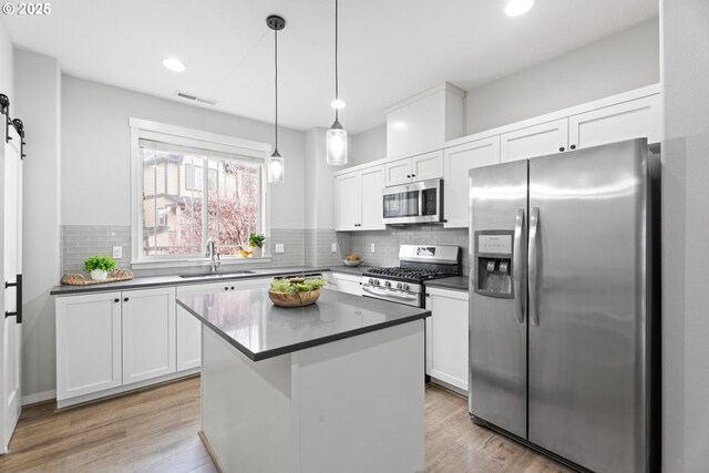 kitchen featuring dark countertops, visible vents, a barn door, appliances with stainless steel finishes, and a sink