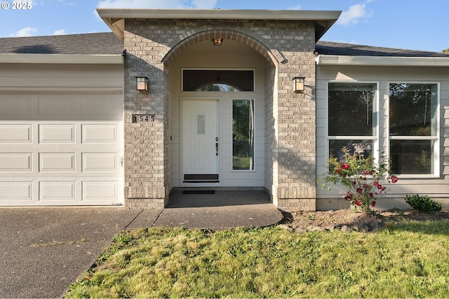 1545 NE Gertz Rd, Portland, OR 97211 - view of exterior entry featuring a garage, roof with shingles, and brick siding