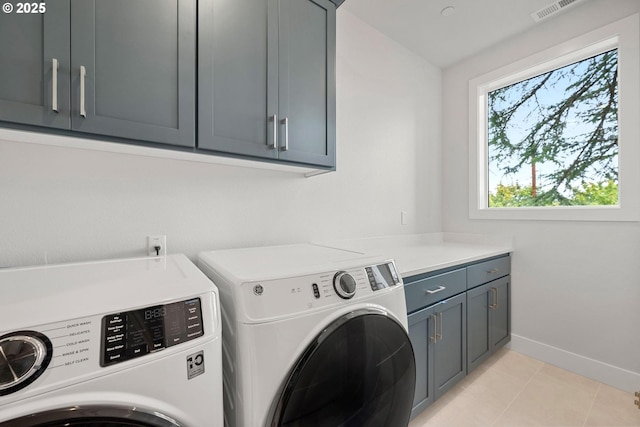 clothes washing area featuring washer and dryer, light tile patterned floors, and cabinets