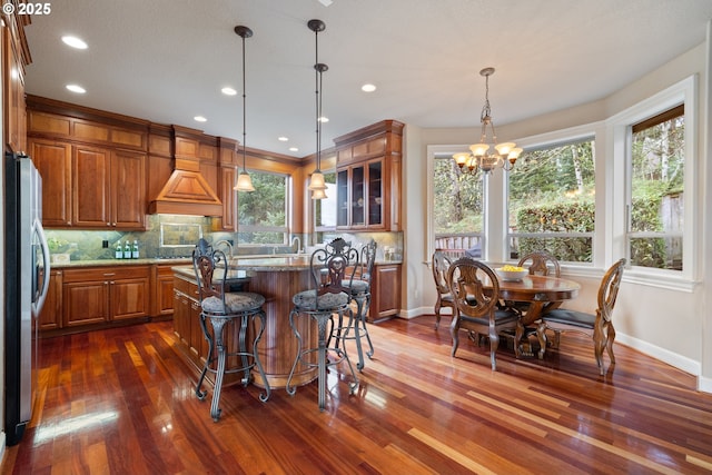14079 SE Alta Vista Dr, Happy Valley, OR 97086 - kitchen with freestanding refrigerator, an inviting chandelier, a center island with sink, brown cabinets, and decorative backsplash