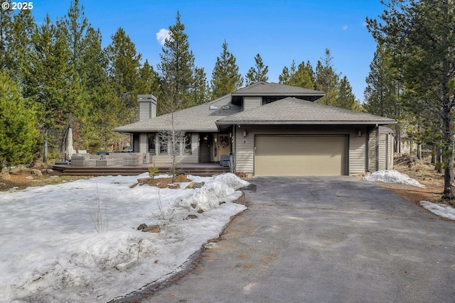 prairie-style home with aphalt driveway, a chimney, an attached garage, and a shingled roof