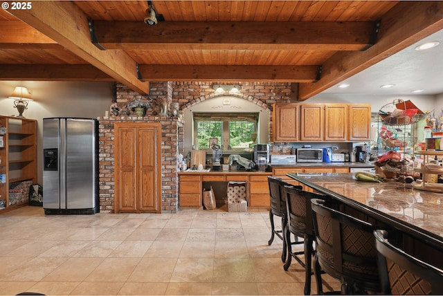 kitchen with beam ceiling, stainless steel fridge with ice dispenser, a breakfast bar area, and dark stone counters