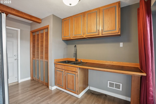 kitchen featuring sink, beamed ceiling, light hardwood / wood-style floors, and a textured ceiling