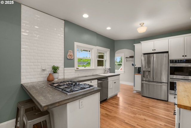 224 NE 44th Ave, Portland, OR 97213 - kitchen featuring stainless steel appliances, backsplash, arched walkways, white cabinets, and light wood-type flooring