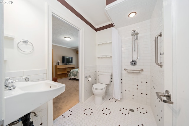 ensuite bathroom with wainscoting, crown molding, tile walls, and toilet