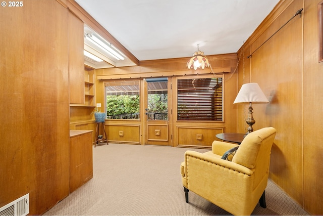 sitting room with ornamental molding, wooden walls, visible vents, and carpet