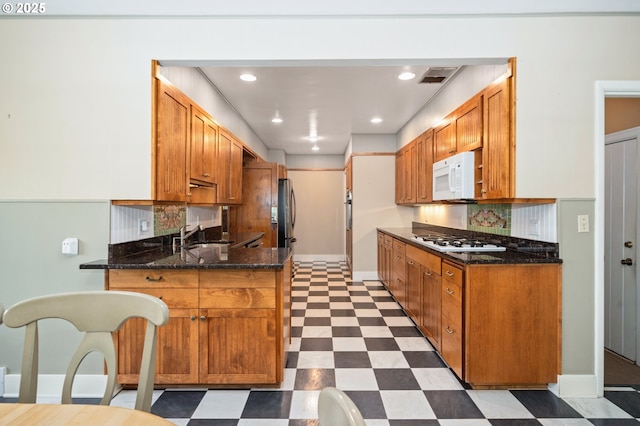 kitchen featuring baseboards, white appliances, a peninsula, dark stone counters, and dark floors