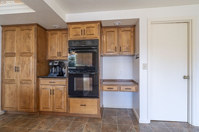 kitchen featuring dobule oven black, brown cabinetry, stone finish flooring, dark countertops, and baseboards