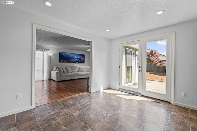 unfurnished living room featuring a textured ceiling, baseboards, stone finish flooring, and recessed lighting
